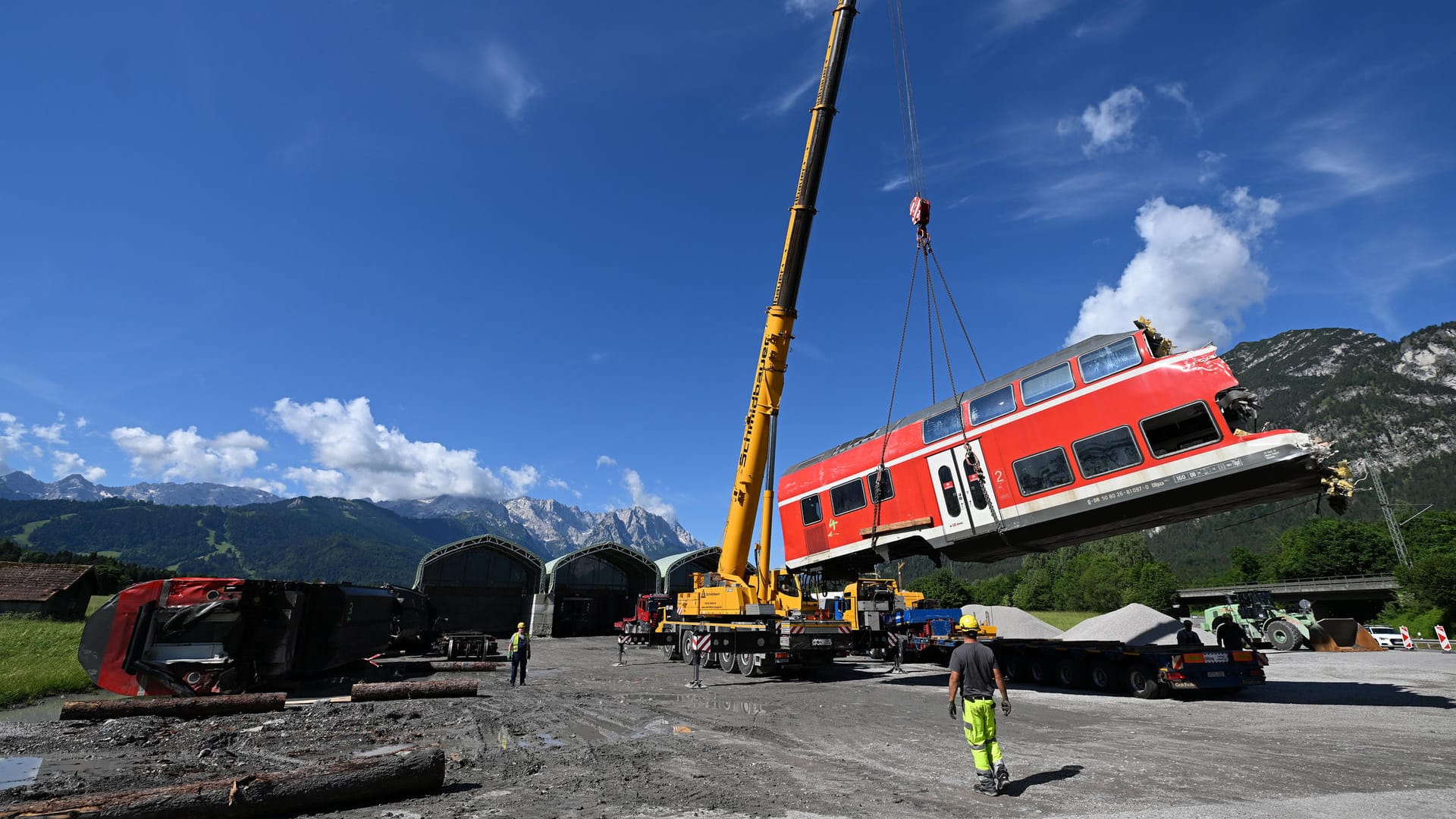 Ein auseinandergeschnittenes Waggonteil wird in einem nahe gelegenen Kieswerk vom Laster gehoben und gelagert. Im Hintergrund ist in der Mitte die Zugspitze zu sehen.