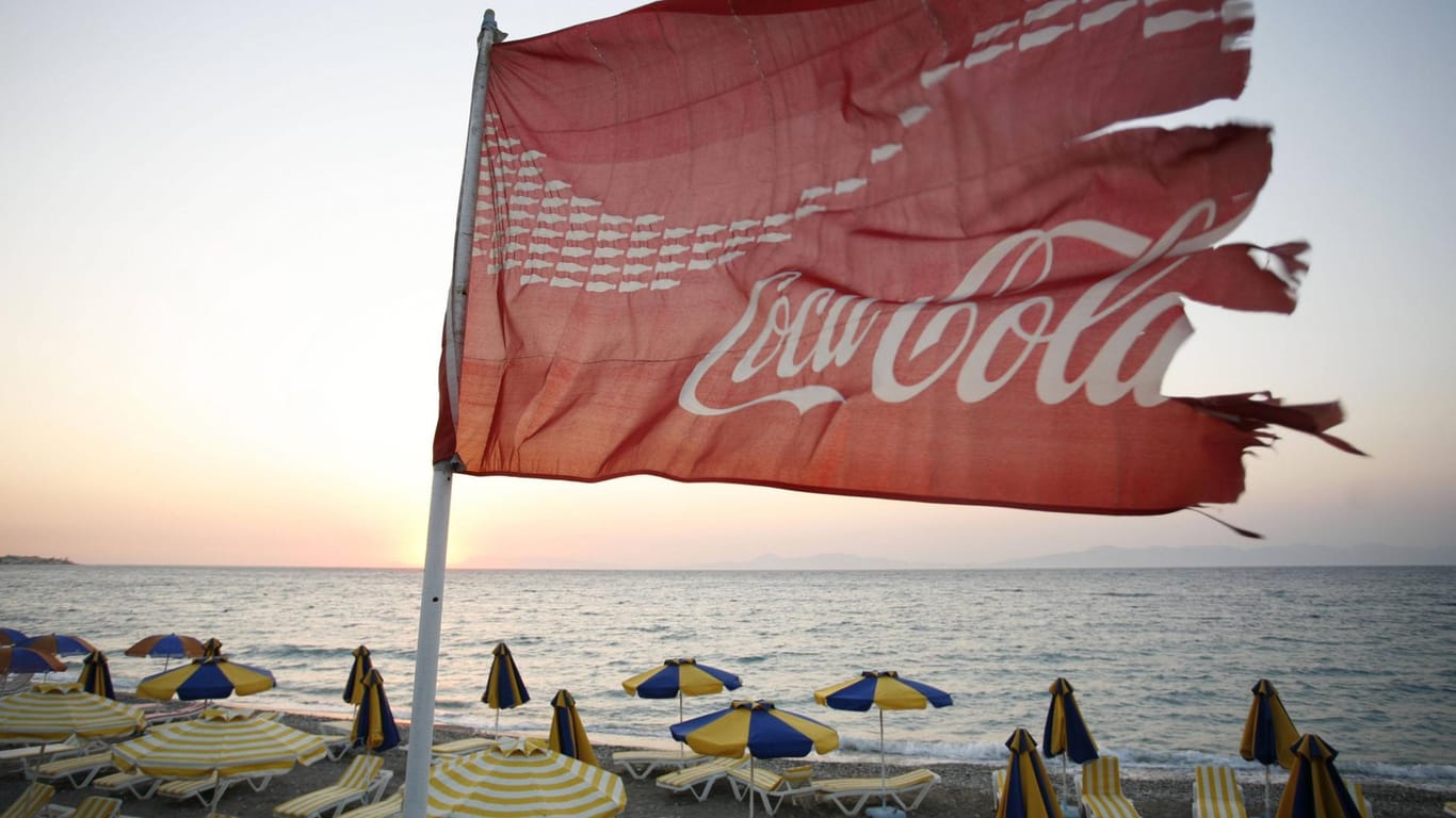 Am Strand von Ixia auf Rhodos flattert eine zerfetzte Coca-Cola-Fahne: Pro Jahr produziert der Getränkehersteller mehr als 100 Milliarden Einweg-Plastikflaschen. Viele davon enden im Meer.