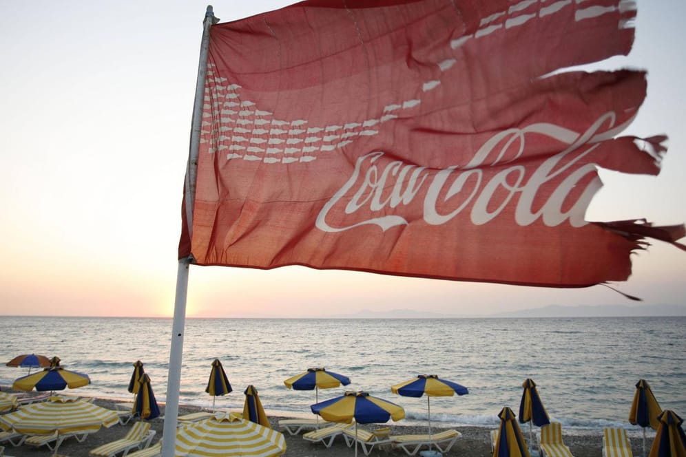 Am Strand von Ixia auf Rhodos flattert eine zerfetzte Coca-Cola-Fahne: Pro Jahr produziert der Getränkehersteller mehr als 100 Milliarden Einweg-Plastikflaschen. Viele davon enden im Meer.
