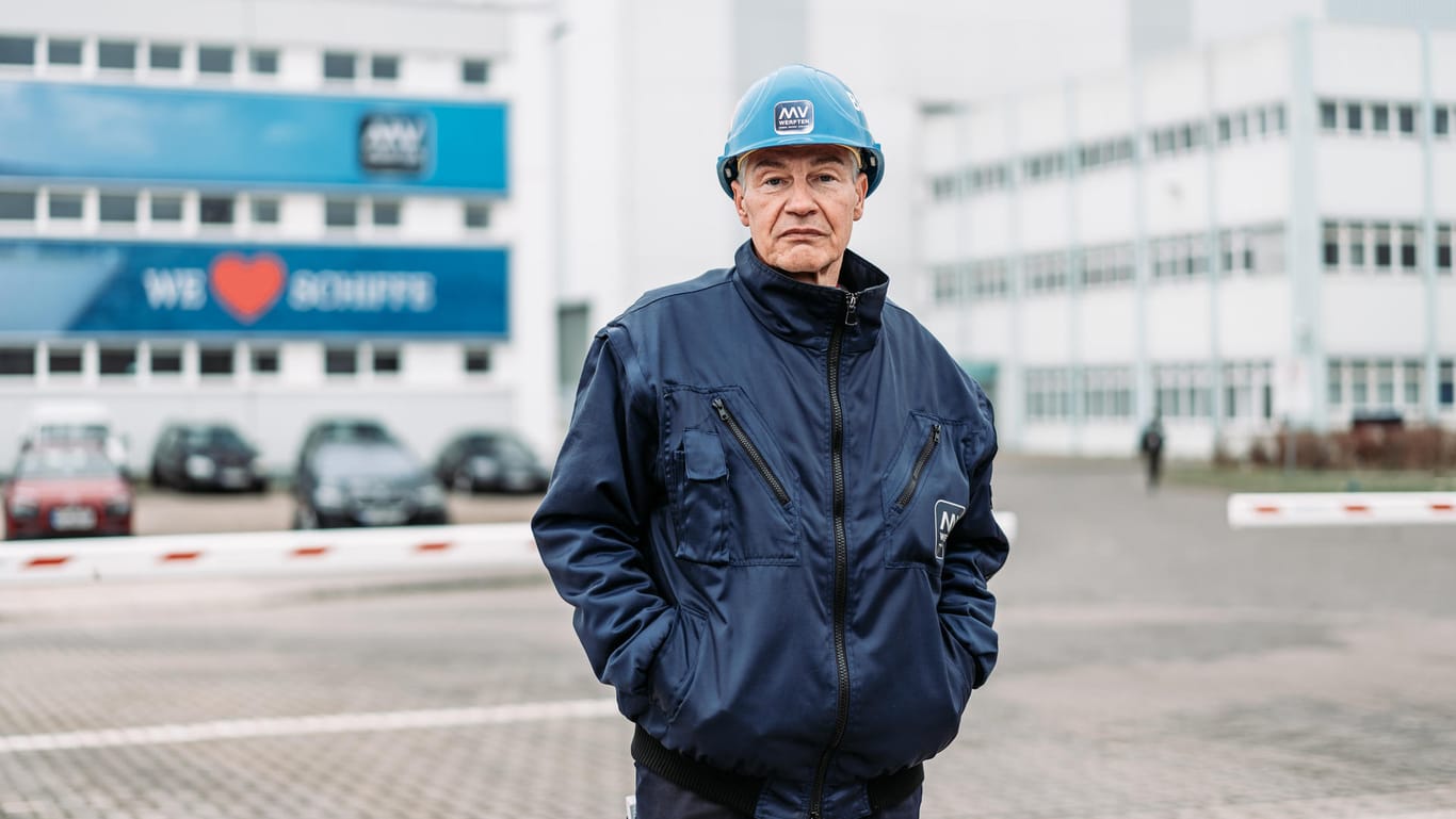 Betriebsrat Folko Manthey steht vor dem Werksgelände in Wismar. In der Halle hinter ihm liegt das größte Kreuzfahrtschiff der Welt.