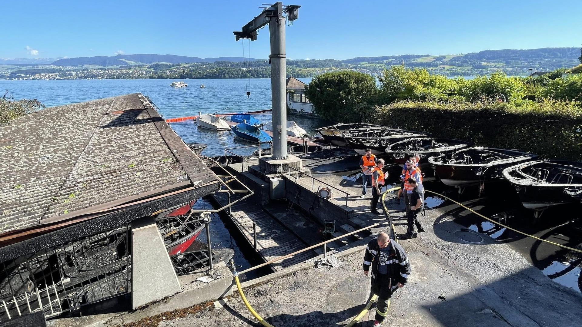 Feuerwehrleute stehen neben den ausgebrannten Booten am Steg: Beim Brand am Zürichsee Feuerwehrleute stehen neben den ausgebrannten Booten am Steg: Beim Brand am Zürichsee