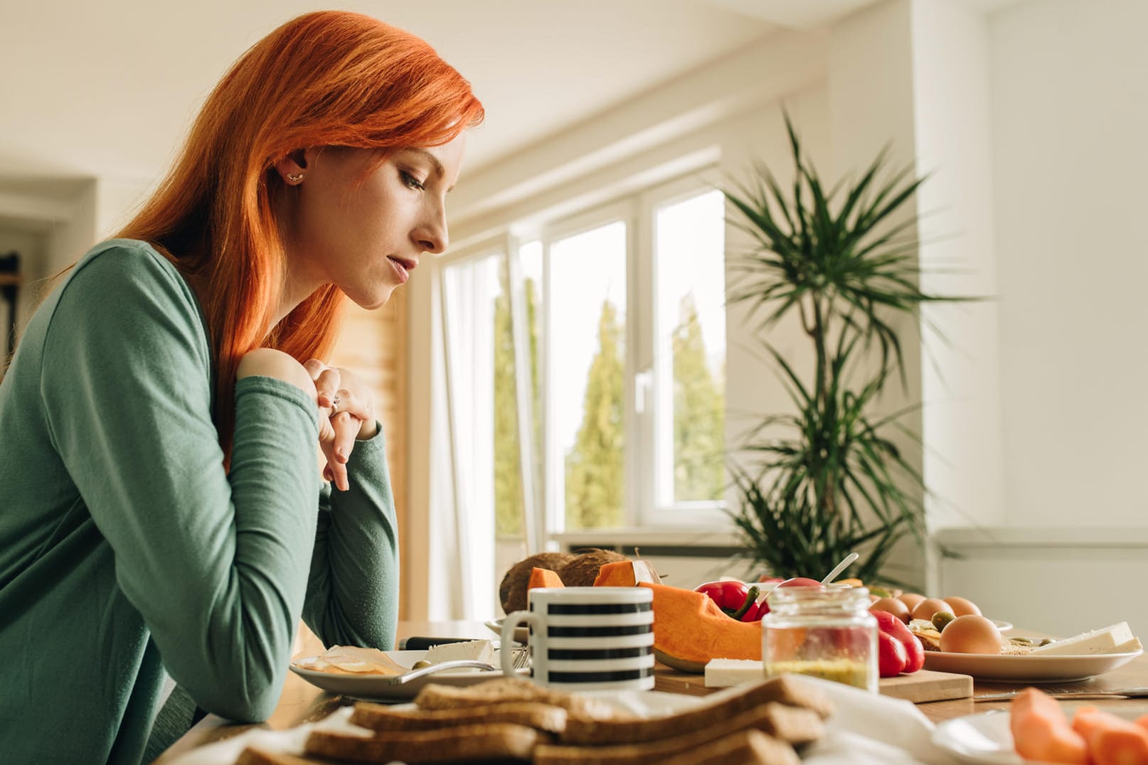 Junge Frau sitzt am Frühstückstisch und schaut nachdenklich auf das Essen.