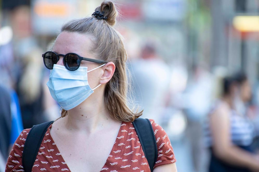 Eine junge Frau mit Sonnenbrille und Mund-Nasen-Schutz (Symbolbild): Derzeit steigen die Corona-Fallzahlen wieder rasant an.