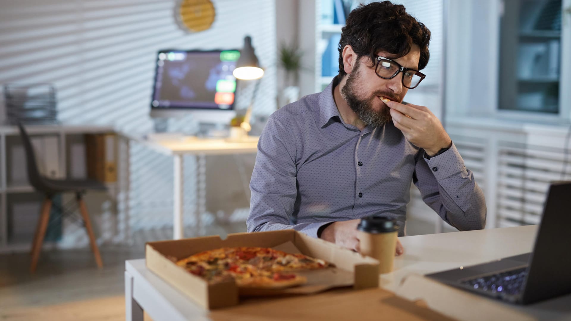 Ein Mann sitzt am Schreibtisch und isst eine Pizza.