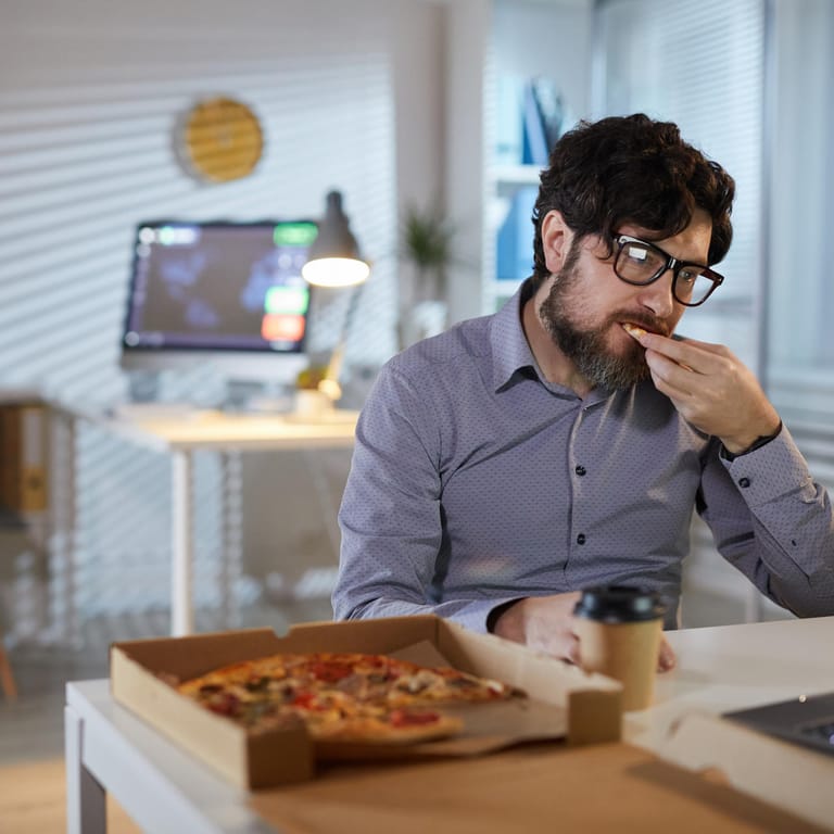 Ein Mann sitzt am Schreibtisch und isst eine Pizza.
