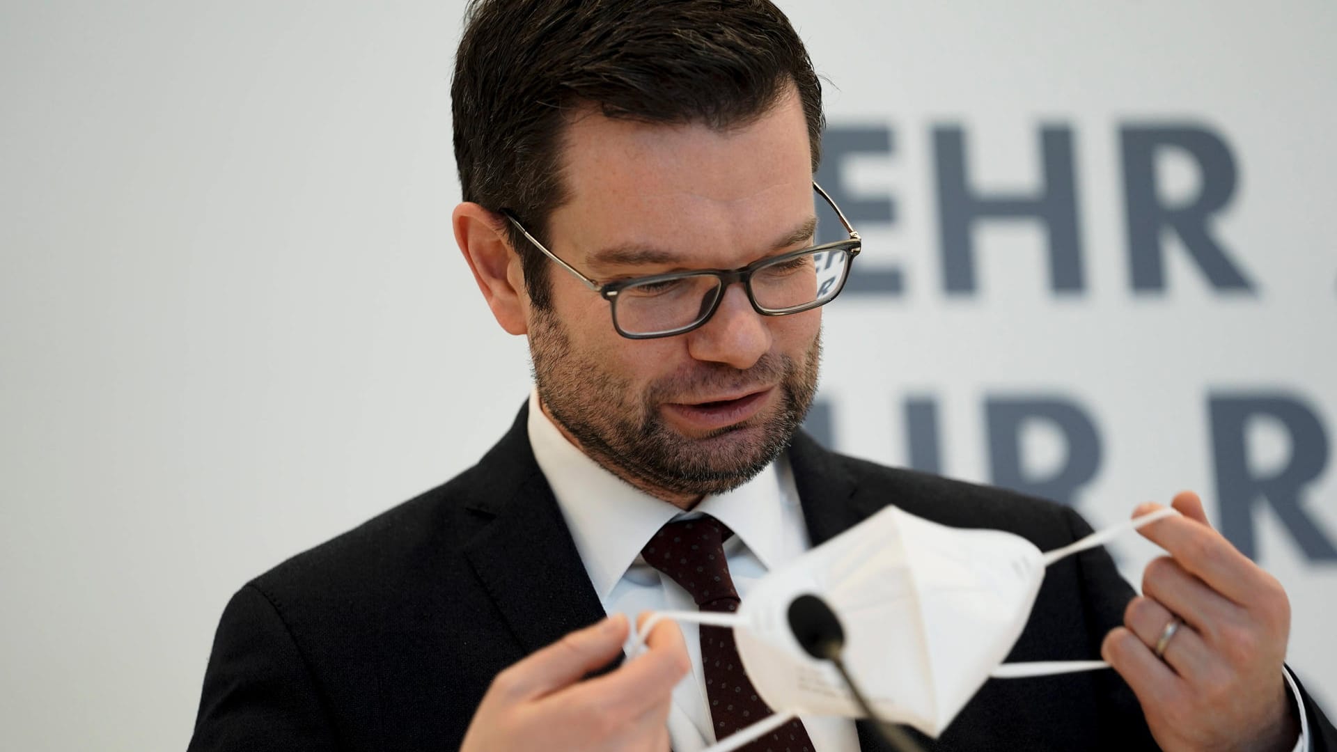 Marco Buschmann hält eine Maske in der Hand (Archivbild): Der Justizminister fordert weitere Gutachten, bevor er eine Maskenpflicht entscheiden will.