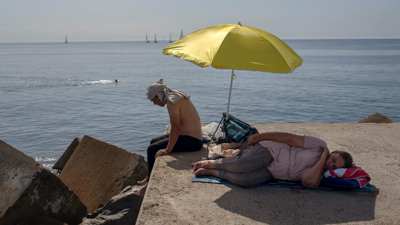 Eine Frau schläft unter einem Schirm auf einem Wellenbrecher vor dem Mittelmeer: Die Menschen suchen Abkühlung.