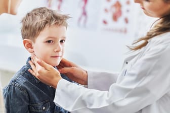Eine Ärztin tastet den Hals eines Jungen ab