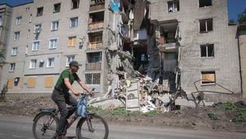 Ukraina, Bakhmut: Mężczyzna przejeżdża rowerem obok budynku zniszczonego przez rosyjskie bombardowania.
