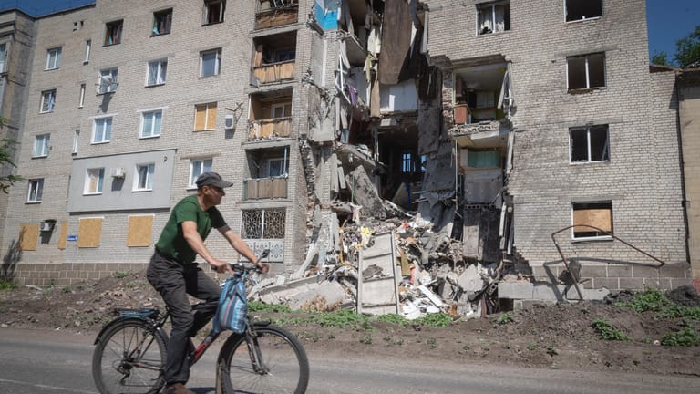 Ukraine, Bachmut: Ein Mann fährt mit dem Fahrrad an einem durch russischen Beschuss beschädigten Gebäude vorbei.