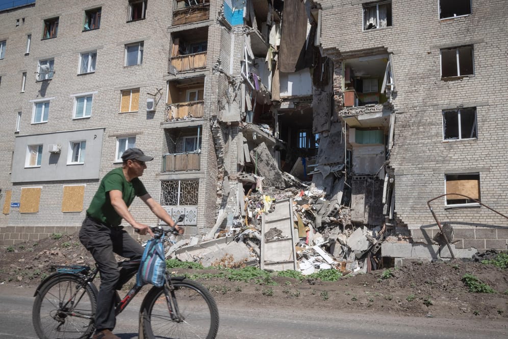 Ukraine, Bachmut: Ein Mann fährt mit dem Fahrrad an einem durch russischen Beschuss beschädigten Gebäude vorbei.