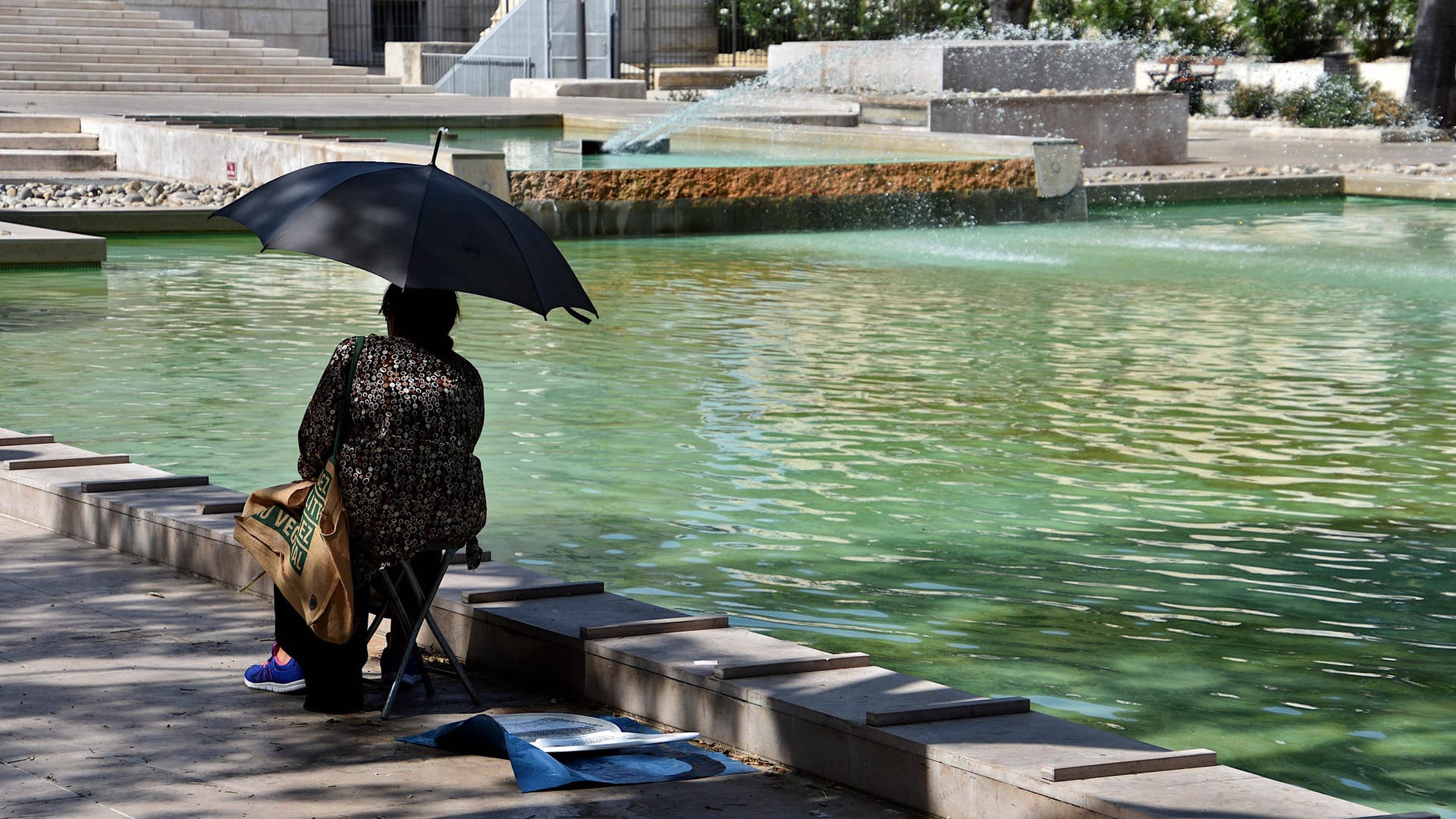 Eine Frau sitzt in Marseille mit Sonnenschirm an einem Teich (Symbolbild): In einigen Regionen Frankreichs herrscht eine Hitzewelle.