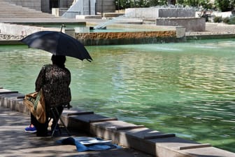 Eine Frau sitzt in Marseille mit Sonnenschirm an einem Teich (Symbolbild): In einigen Regionen Frankreichs herrscht eine Hitzewelle.