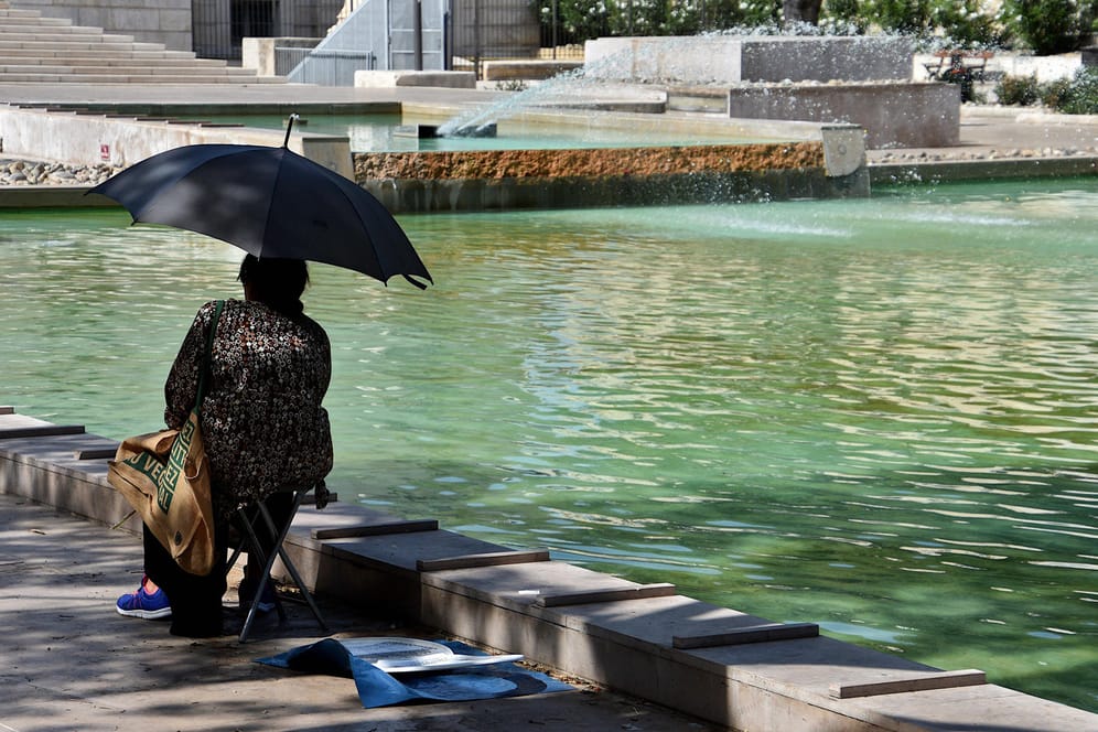 Eine Frau sitzt in Marseille mit Sonnenschirm an einem Teich (Symbolbild): In einigen Regionen Frankreichs herrscht noch immer Dürre.