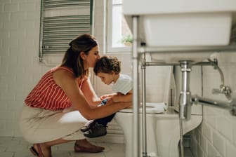 Eine Frau hilft einem kleinen Jungen auf der Toilette.