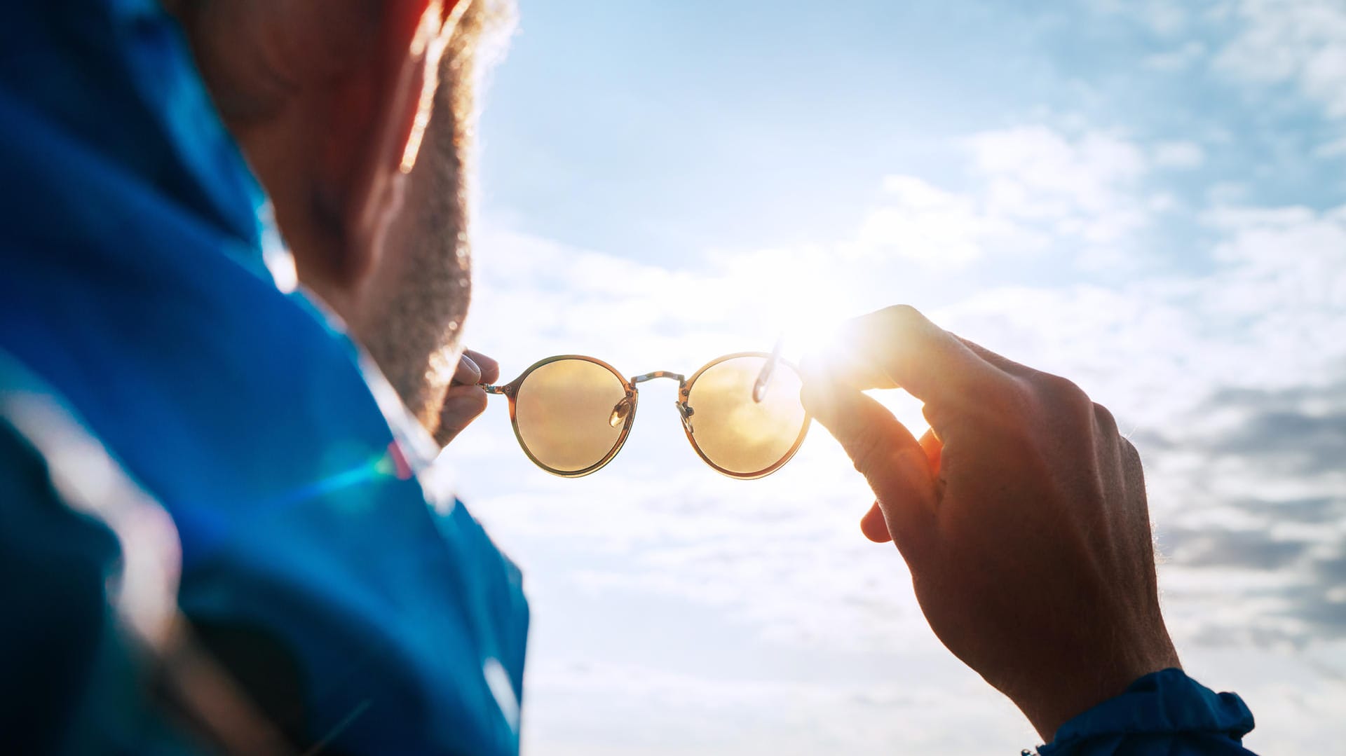 Mann in den Bergen betrachtet seine Sonnenbrille im Sonnenlicht.