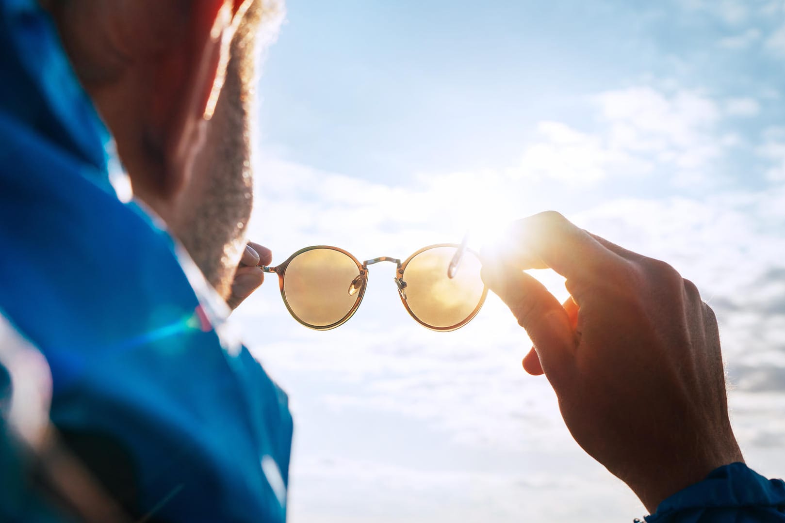 Mann in den Bergen betrachtet seine Sonnenbrille im Sonnenlicht.