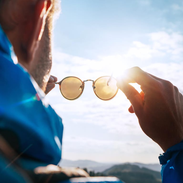 Mann in den Bergen betrachtet seine Sonnenbrille im Sonnenlicht.