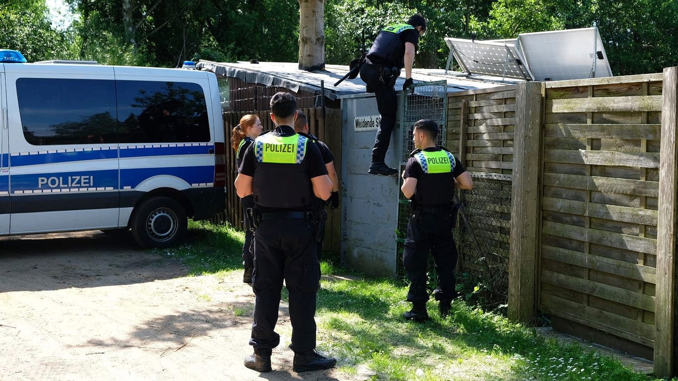 Ein Polizist klettert in einen der Kleingärten: In Bergedorf wird nach einer verletzten Person gesucht.