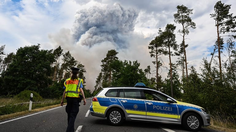 Ein Polizeiauto sperrt die Straße ab: Ein munitionsbelastetes Waldstück brennt.