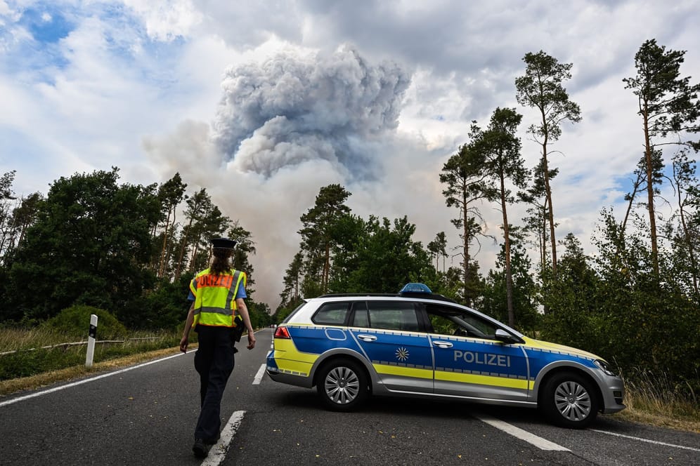 Ein Polizeiauto sperrt die Straße ab: Ein munitionsbelastetes Waldstück brennt.