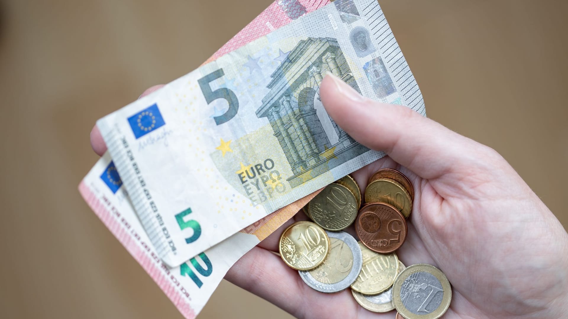 Eine Frau hält zwei Geldscheine und ein paar Münzen in der Hand Eine Frau hält zwei Geldscheine und ein paar Münzen in der Hand