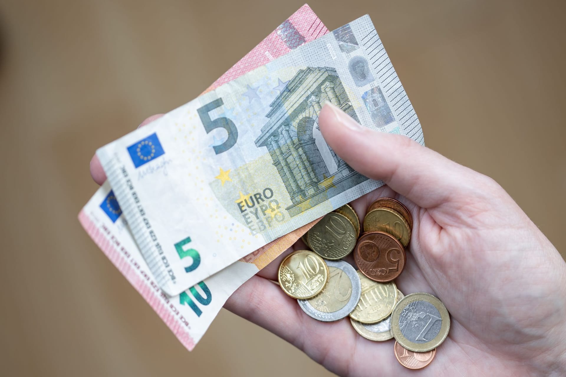 Eine Frau hält zwei Geldscheine und ein paar Münzen in der Hand