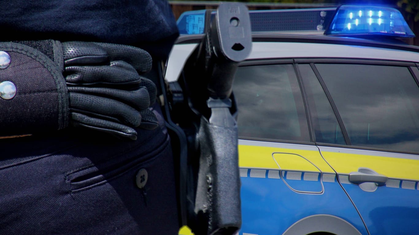Polizist mit Waffe vor Streifenwagen (Symbolbild): Bei den Taten wurde mehrfach Gebrauch von Schusswaffen gemacht.
