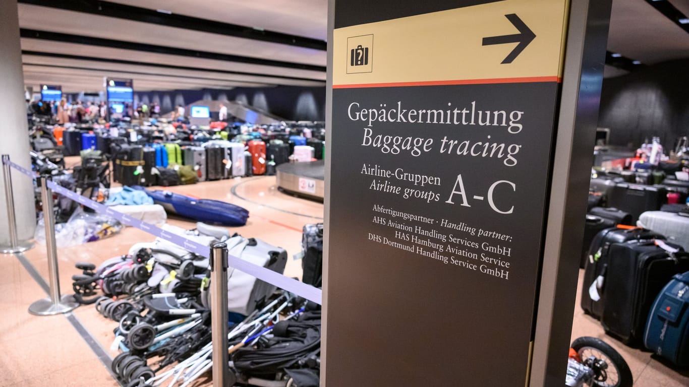"Gepäckermittlung" steht auf einem Hinweisschild vor zahlreichen lagernden Koffern und zusammengeklappte Kinderwagen im Gepäckausgabe-Bereich.