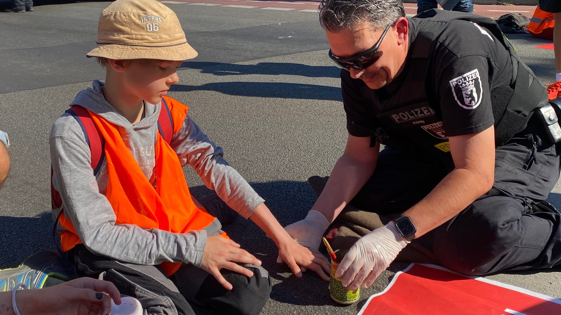 Ein Polizist versucht den 12-jährigen Simeon von der Straße zu bringen: Er und die 15-jährige Rebekka haben sich auf der Fahrbahn der A100 in Berlin festgeklebt.