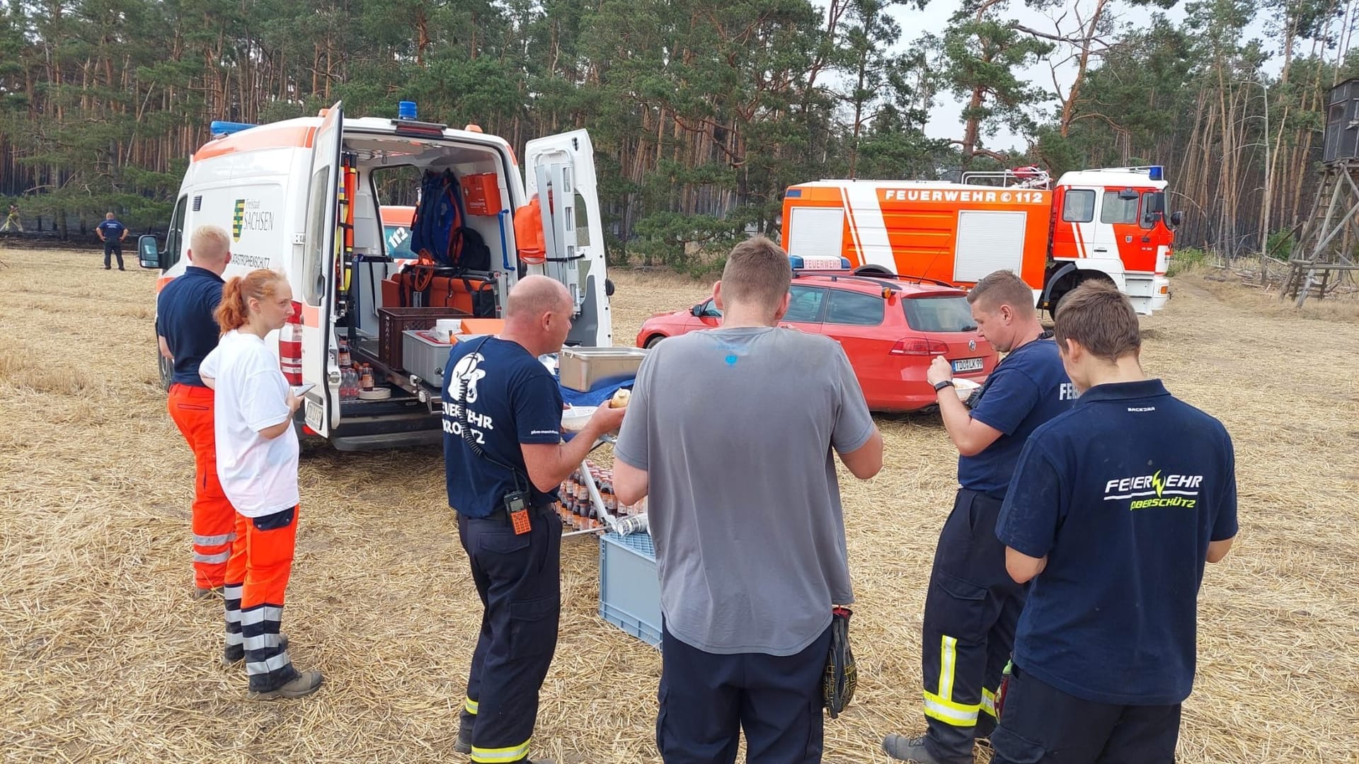 Männer der Freiwilligen Feuerwehr bei einer Pause: Das Rote Kreuz versorgt die abgekämpften Einsatzkräfte mit Essen und Trinken.