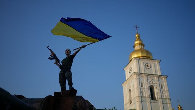 Eine Frau schwenkt die ukrainische Flagge auf einem zerstörten russischen Panzer in Kiew.