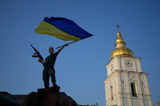 Eine Frau schwenkt die ukrainische Flagge auf einem zerstörten russischen Panzer in Kiew.