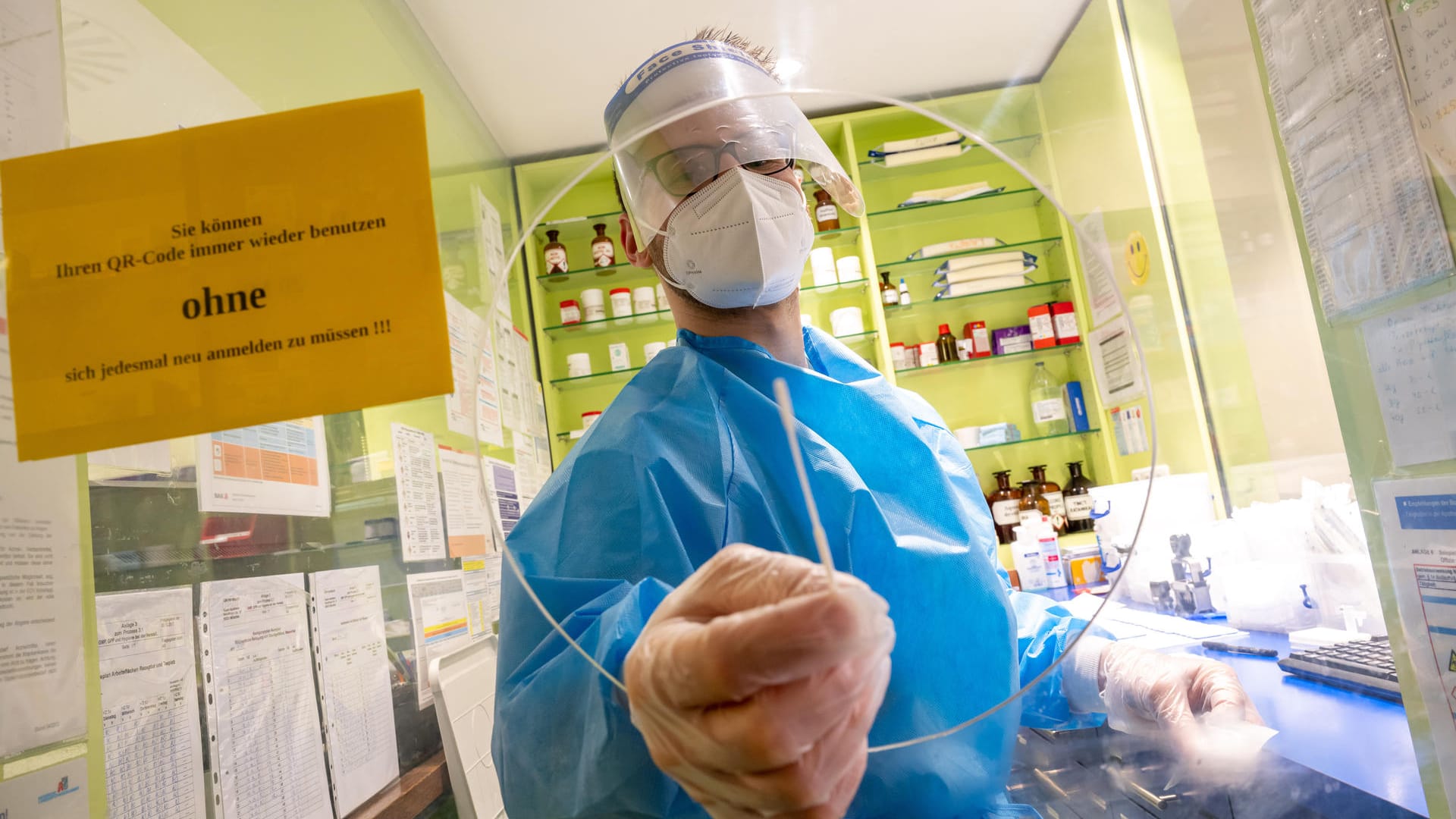 Ein Mitarbeiter einer Apotheke in der Innenstadt hält ein Teststäbchen für einen Corona-Schnelltest durch die Öffnung einer Scheibe.