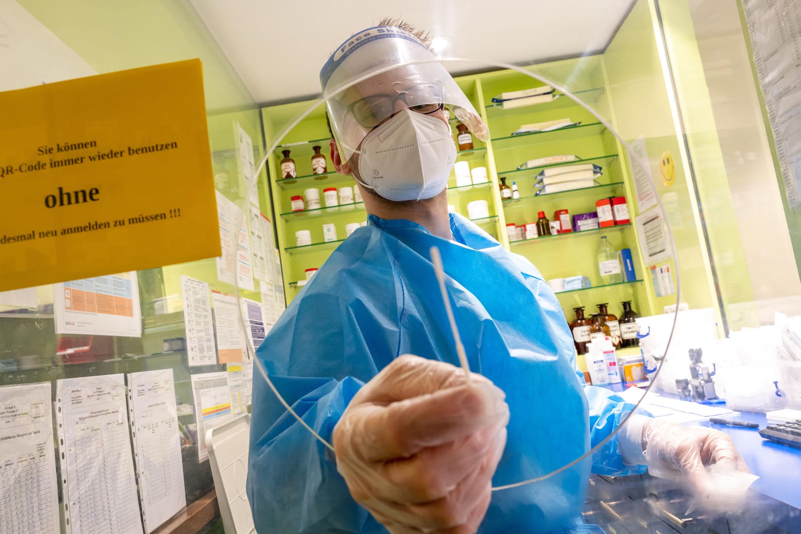 Ein Mitarbeiter einer Apotheke in der Innenstadt hält ein Teststäbchen für einen Corona-Schnelltest durch die Öffnung einer Scheibe.