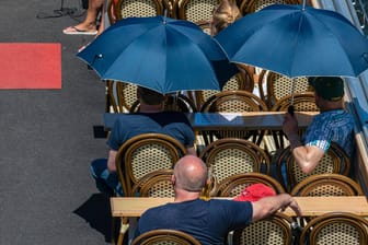 Menschen schützen sich mit Regenschirmen vor der Sonne: Hohe Temperaturen können das Herz-Kreislauf-System stark belasten.