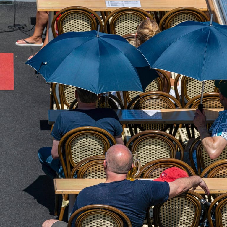 Menschen schützen sich mit Regenschirmen vor der Sonne: Hohe Temperaturen können das Herz-Kreislauf-System stark belasten.