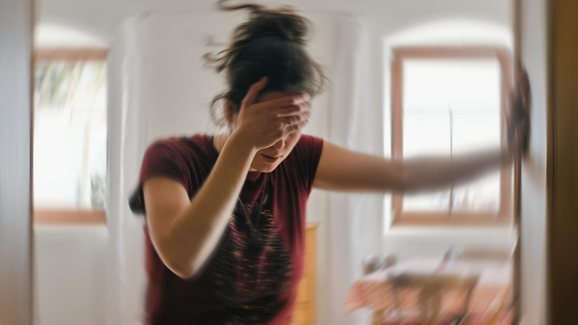 Eine Frau mit Schwindelattacke hält sich am Türrahmen fest.