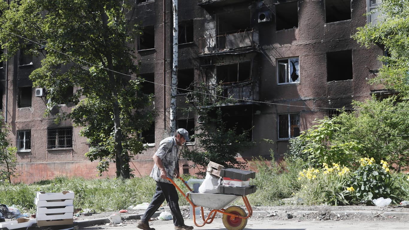 Ein Mann schiebt einen Schubkarren vor einem zerstörten Haus in Mariupol (Archivbild): Die Ukraine ruft nach Wiederaufbauhilfe.