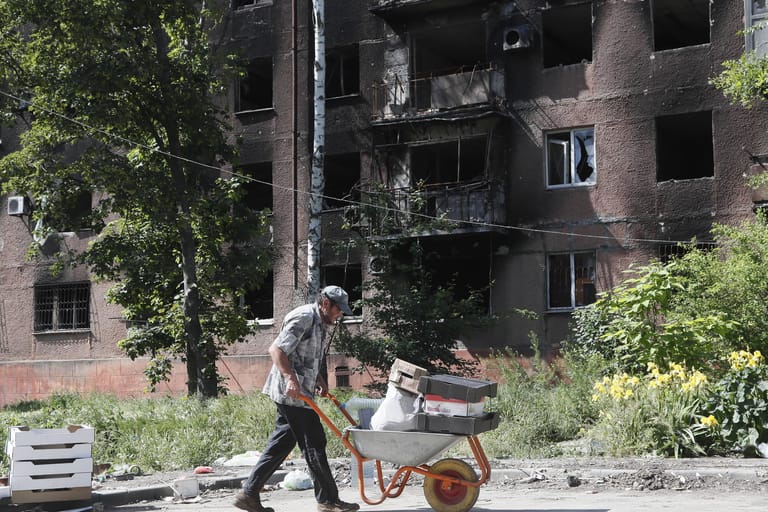 Ein Mann schiebt einen Schubkarren vor einem zerstörten Haus in Mariupol (Archivbild): Die Ukraine ruft nach Wiederaufbauhilfe.
