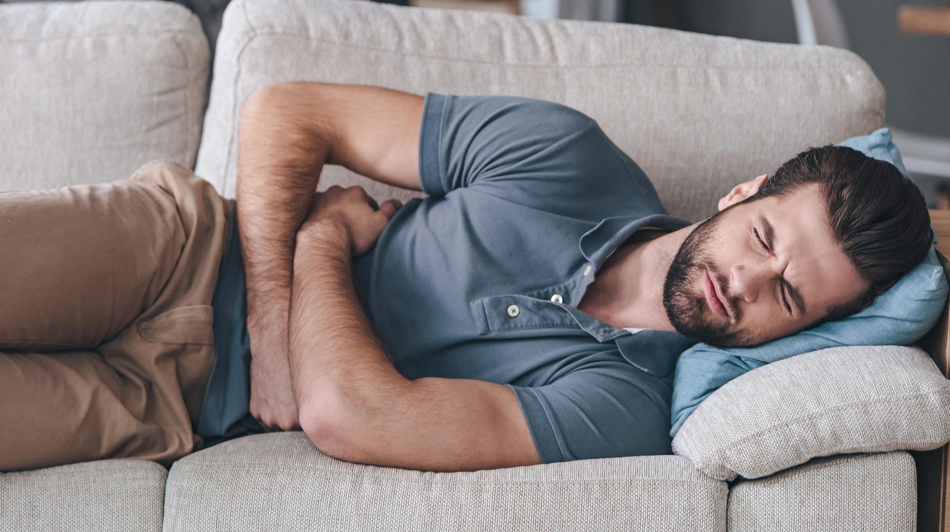 Ein Mann liegt mit starken Schmerzen auf dem Sofa.