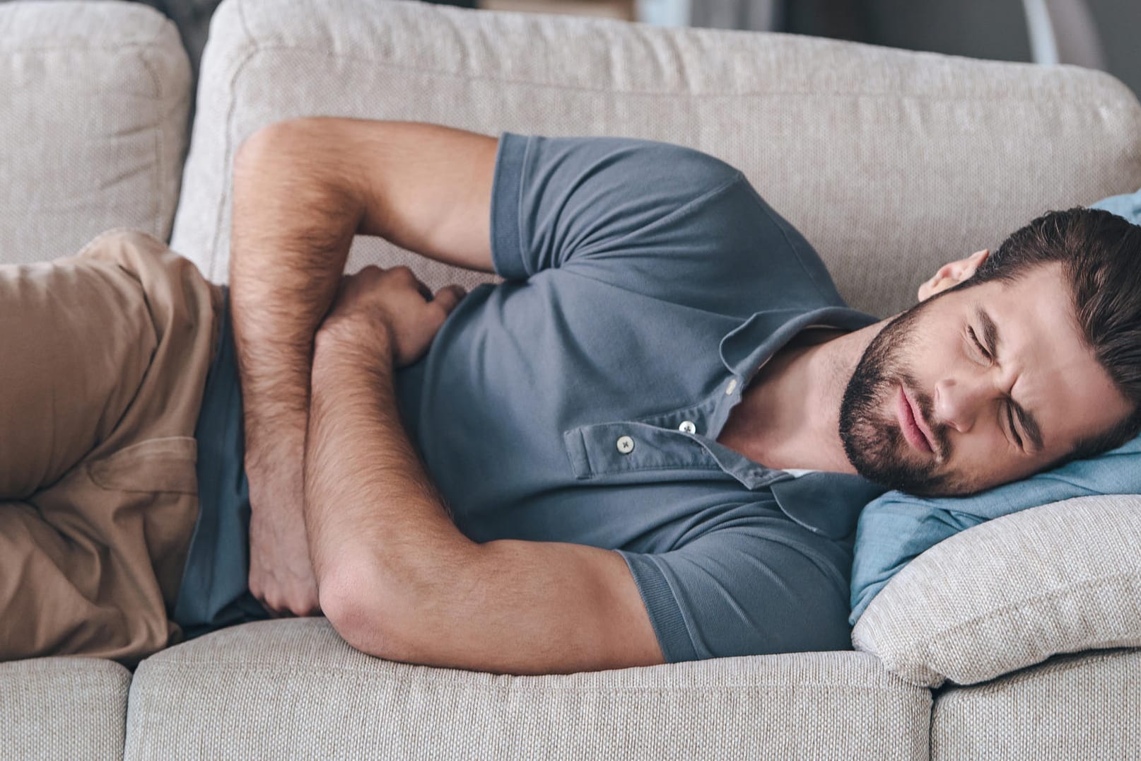 Ein Mann liegt mit starken Schmerzen auf dem Sofa.