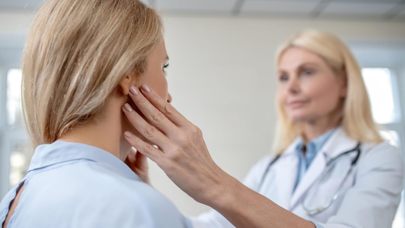 Ärztin tastet die Region der Ohren bei einer Patientin ab.