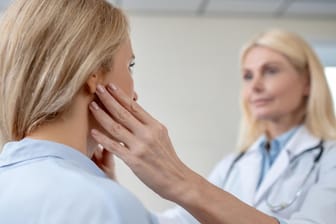 Ärztin tastet die Region der Ohren bei einer Patientin ab.