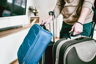 Eine Person trägt mehrere Koffer gleichzeitig: Schwer schleppen muss nicht sein – man kann sein Gepäck in den Urlaub auch einfach vorreisen lassen.
