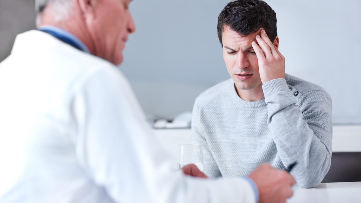 Mann mit Kopfschmerzen bei Arzt: Eine Aura-Migräne sollte immer von einem Arzt abgeklärt werden. Denn die Symptome ähneln teilweise denen eines Schlaganfalls.
