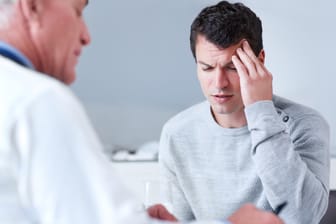 Mann mit Kopfschmerzen beim Arzt