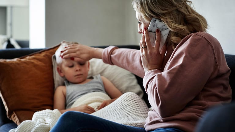 Mutter telefoniert, während sie bei ihrem kranken Sohn am Bett sitzt.