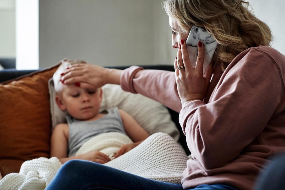 Mutter telefoniert, während sie bei ihrem kranken Sohn am Bett sitzt.
