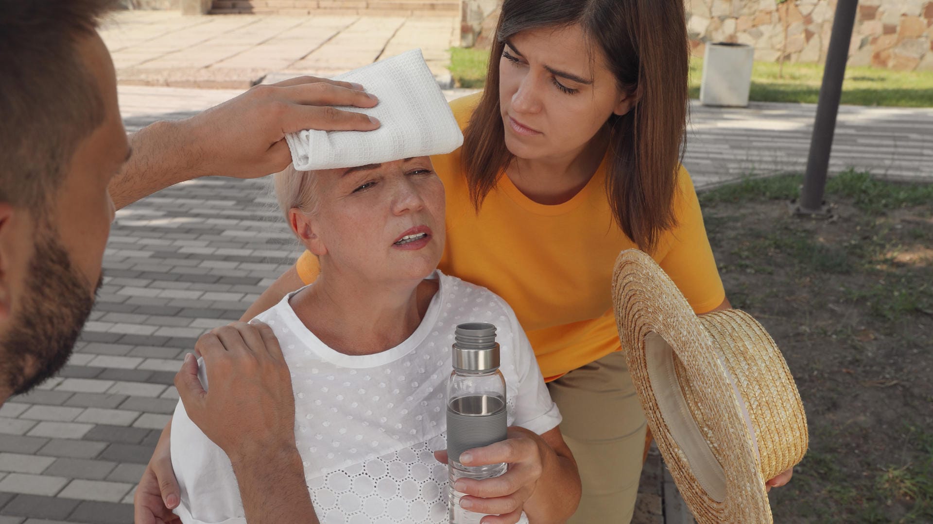 Ältere Frau mit Kreislaufproblem wird von einer Frau und einem Mann betreut.